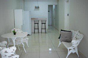 A compact living space with a kitchenette, a dining table with chairs, and a white sofa. - Hospedaria Valdice Damasceno (Piranhas)