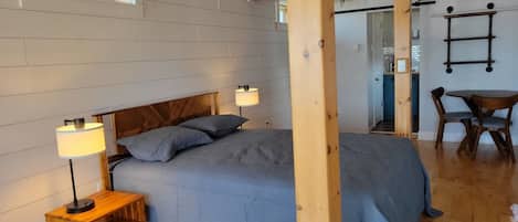 A bedroom with a bed, bedside lamps, a wooden headboard, and a dining area with a table and chairs.
