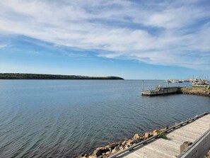 A calm waterfront with a wooden dock extending into the water, a small pier with boats, and a distant landmass.