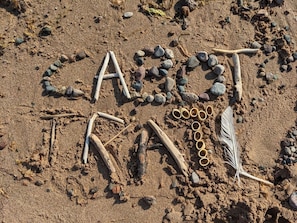 A sandy surface with rocks and sticks arranged to spell 'CASOT' and 'MAL.' - The Sunset Harbour Village Suite (Chéticamp)