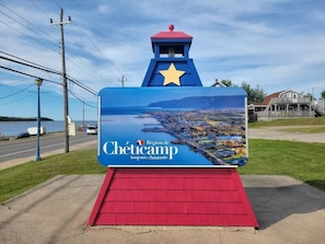 A sign with a view of a coastal town and a star on top. - The Sunset Harbour Village Suite (Chéticamp)