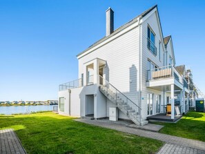 Ein modernes, zweistöckiges Haus mit Balkon, Treppe und Blick auf ein Gewässer.
