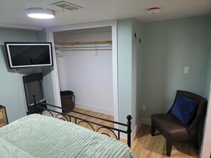 Ein Schlafzimmer mit Bett, Sessel, Fernseher, Schrank und Rauchmelder an der Decke.