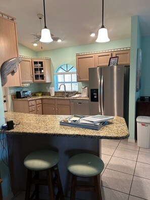 A kitchen with a granite countertop, stainless steel appliances, wooden cabinets, and a window with blinds. - Manatee Manor 3/2 House on Lake Sebring! (Sebring)