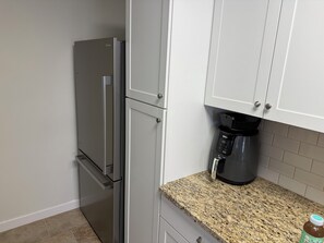 Eine Küche mit einem Edelstahlkühlschrank, einer Kaffeemaschine und einer Arbeitsplatte aus Granit.
