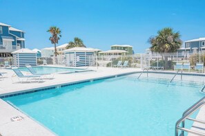 En swimmingpool med solstolar och ett inhägnat område, omgiven av byggnader med en enhetlig arkitektonisk stil.