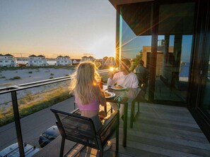 Ein Essbereich mit Blick auf den Strand und Häuser, der moderne Architektur mit Glas- und Metallelementen aufweist.