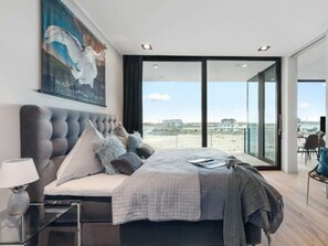 Ein modernes Schlafzimmer mit einem großen Bett, Blick auf den Strand und einem Essbereich.