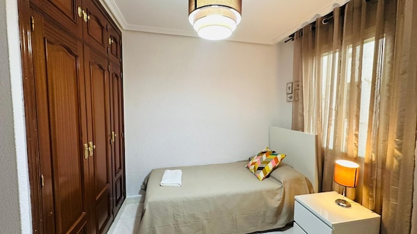 A hotel room with a bed, a bedside table with a lamp, a wardrobe, and a ceiling light fixture.