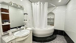 Ein modernes Badezimmer mit einer großen Badewanne, einem Waschtisch mit Spiegel und einer Duschvorhang.