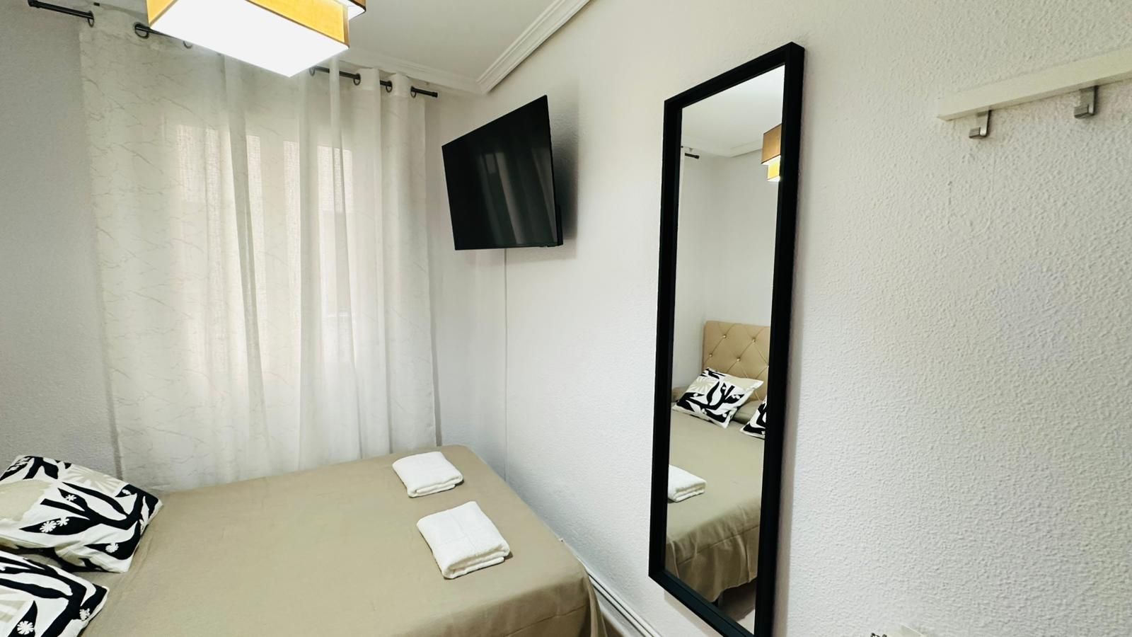A hotel room with a bed, a large mirror, and a TV mounted on the wall.