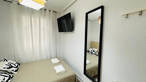 A hotel room with a bed, a large mirror, and a TV mounted on the wall.