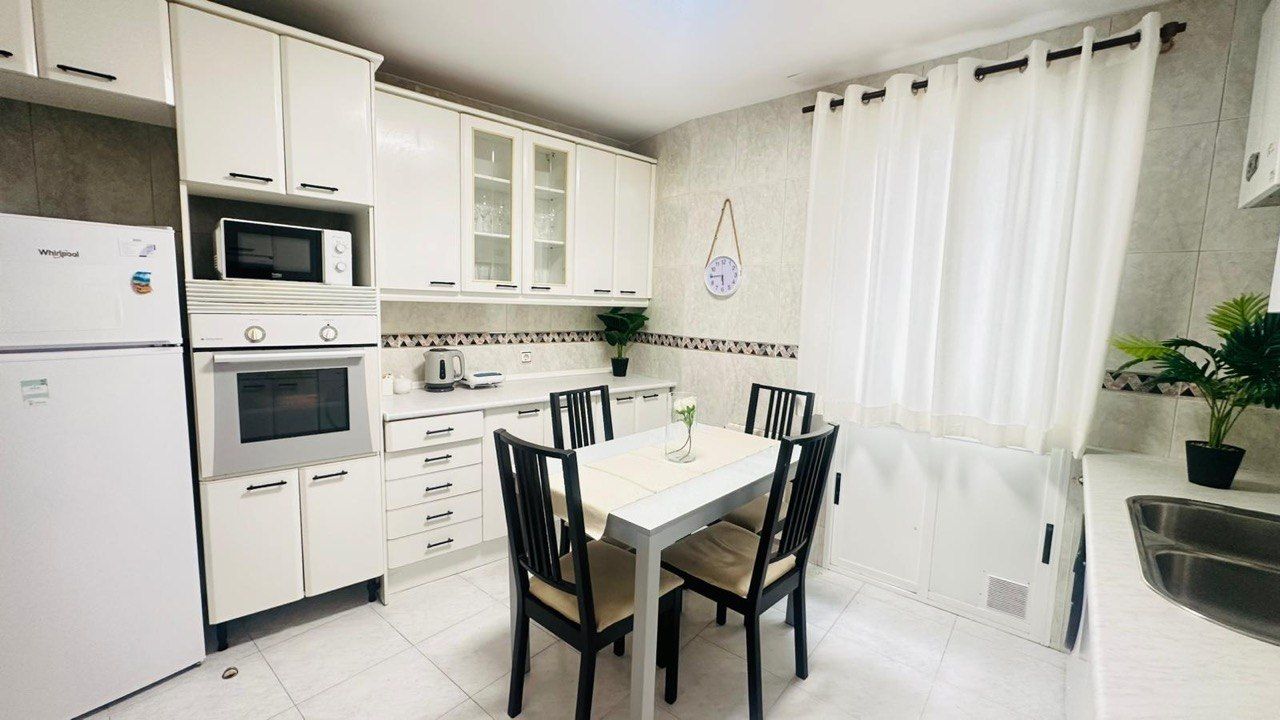 A compact kitchen with white cabinetry, a microwave, an oven, a sink, and a dining area with a table and chairs.