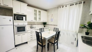 A compact kitchen with white cabinetry, a microwave, an oven, a sink, and a dining area with a table and chairs.