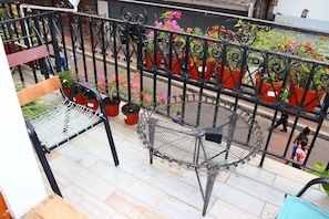Ein Balkon mit einem Metallstuhl, einem kleinen Tisch und Pflanzen in Töpfen.