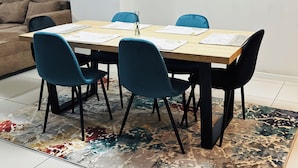A dining area with a wooden table, four blue chairs, and a patterned rug. - Apartment in Sandton (Sandton)