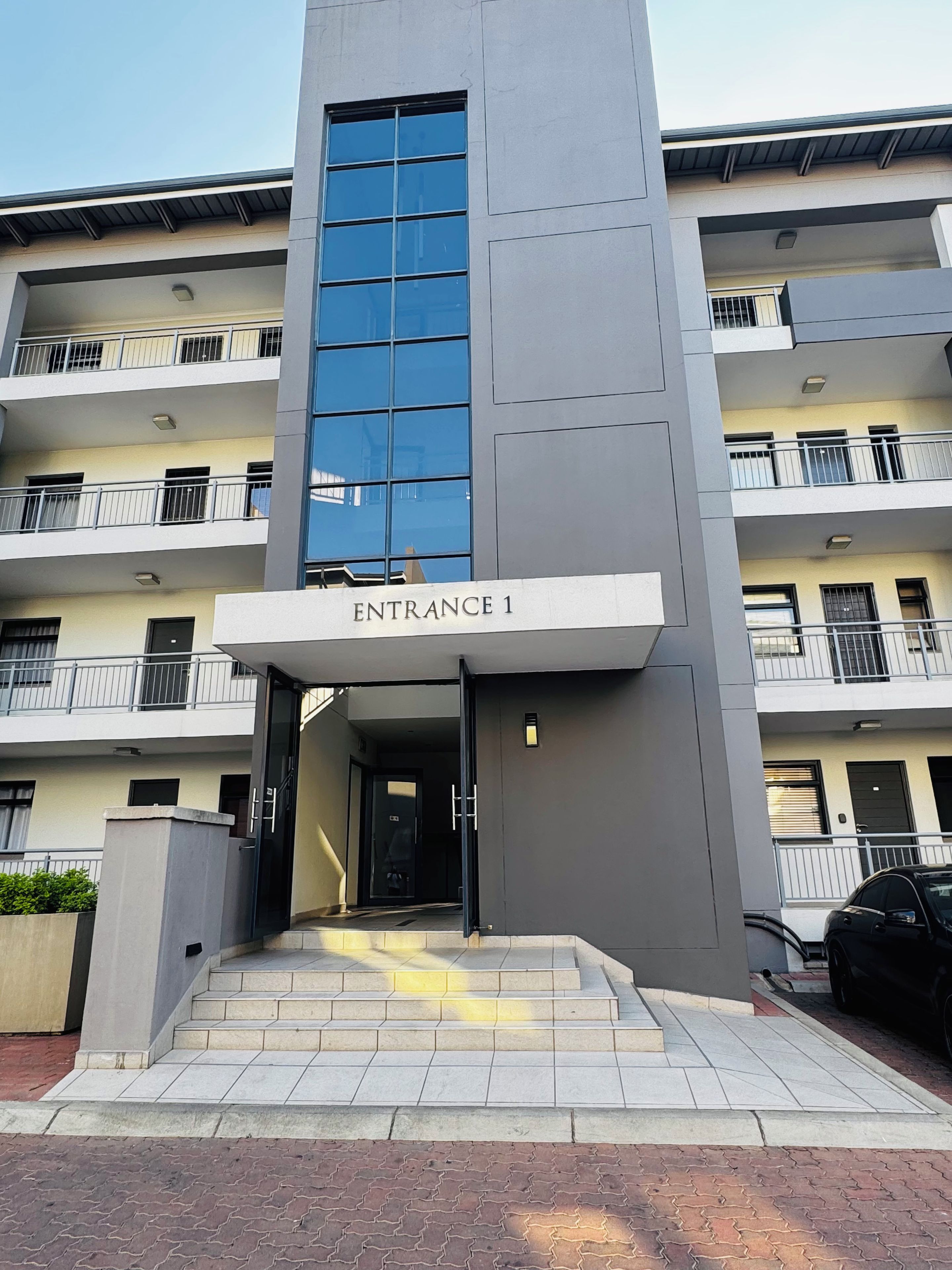 A modern building with a prominent entrance labeled 'Entrance 1,' featuring a staircase leading up to the door.