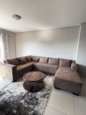 A modern living room with a sectional sofa, a round coffee table, and a patterned rug. - Apartment in Sandton (Sandton)
