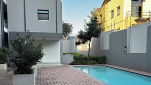 A swimming pool area with a brick pathway, a modern building, and a tree. - Apartment in Sandton (Sandton)