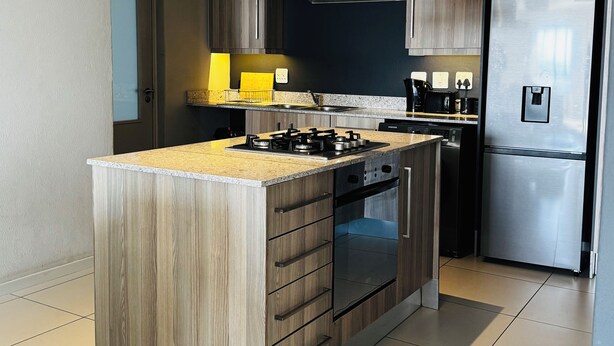 A modern kitchen with a central island, built-in oven, stainless steel appliances, and a large refrigerator. - Apartment in Sandton (Sandton)