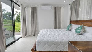 Un dormitorio con una cama grande, cabecera de madera y vista a un jardín por un ventanal corredero.