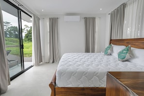 Un dormitorio con una cama grande, cabecera de madera y vista a un jardín por un ventanal corredero.