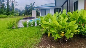 Una casa moderna con piscina, rodeada de vegetación exuberante y un césped cuidado.