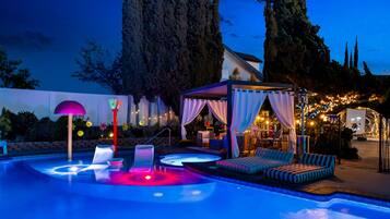 A swimming pool area with lounge chairs and a covered seating area at dusk.