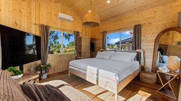 Un dormitorio de cabaña de madera con una cama, un televisor, un ventanal y vistas al exterior.