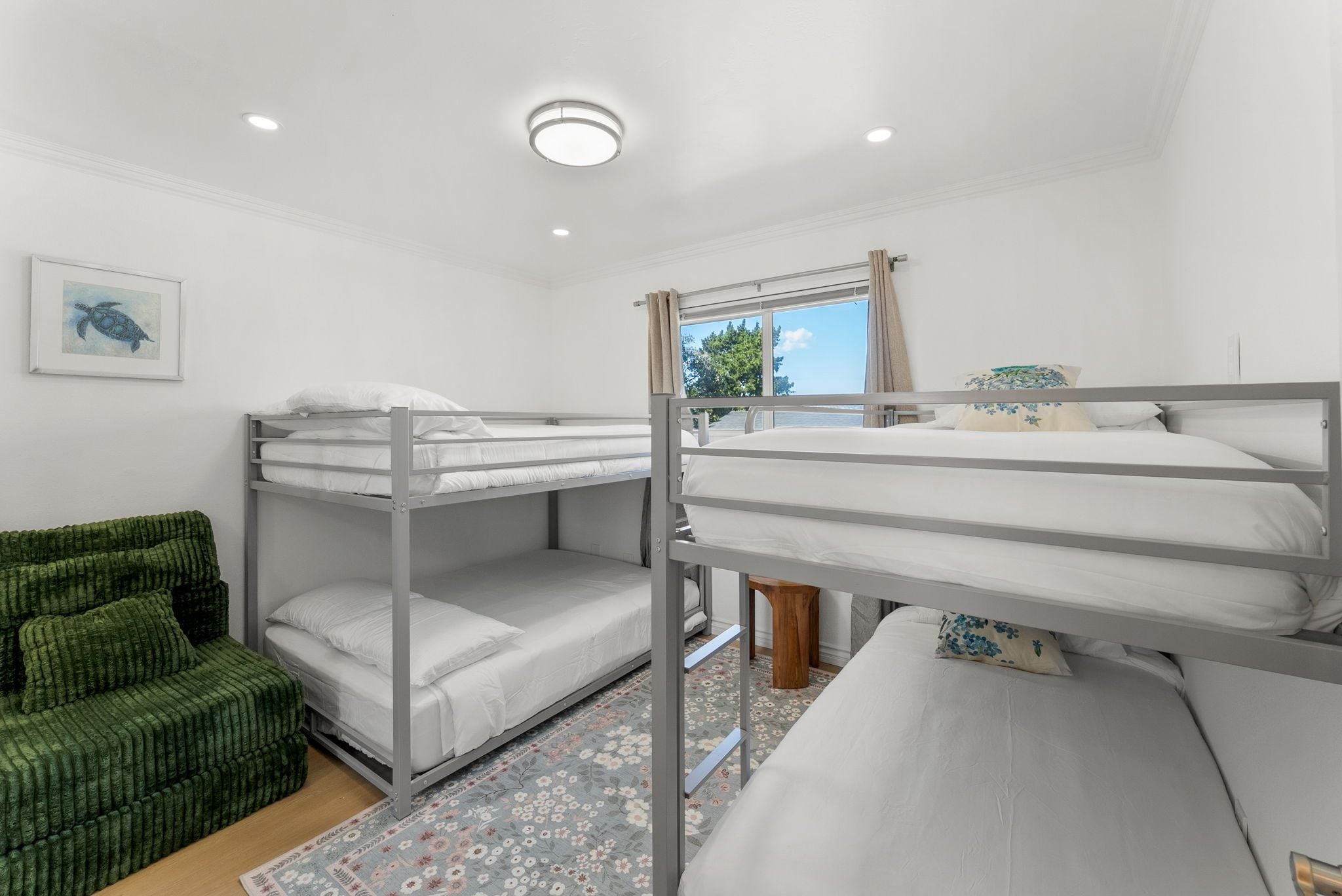 A bunk bed room with a green upholstered sofa, a framed picture on the wall, and a window with curtains.