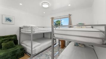 A bunk bed room with a green upholstered sofa, a framed picture on the wall, and a window with curtains.