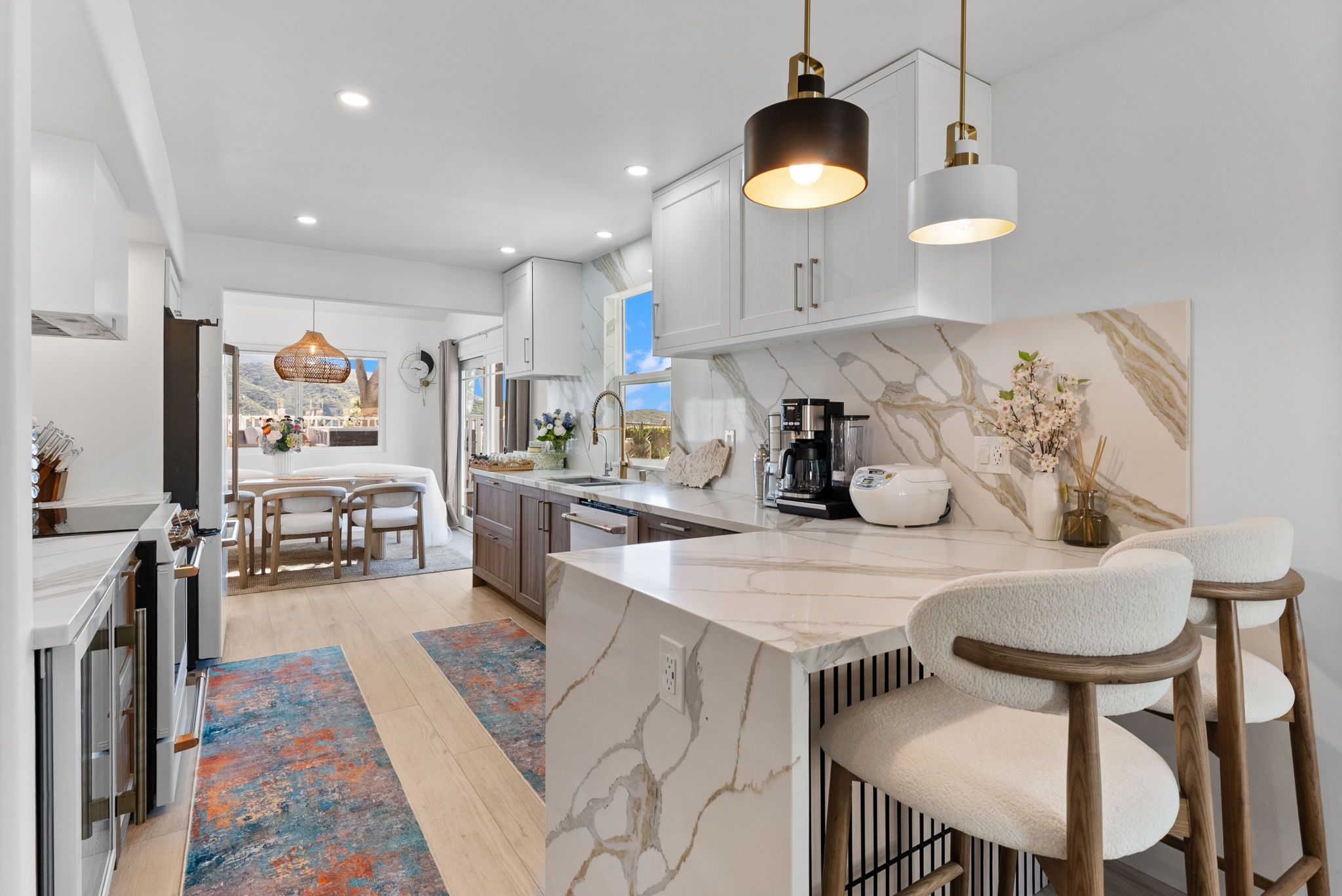 A modern kitchen with marble countertops, pendant lighting, and a view to the outside.