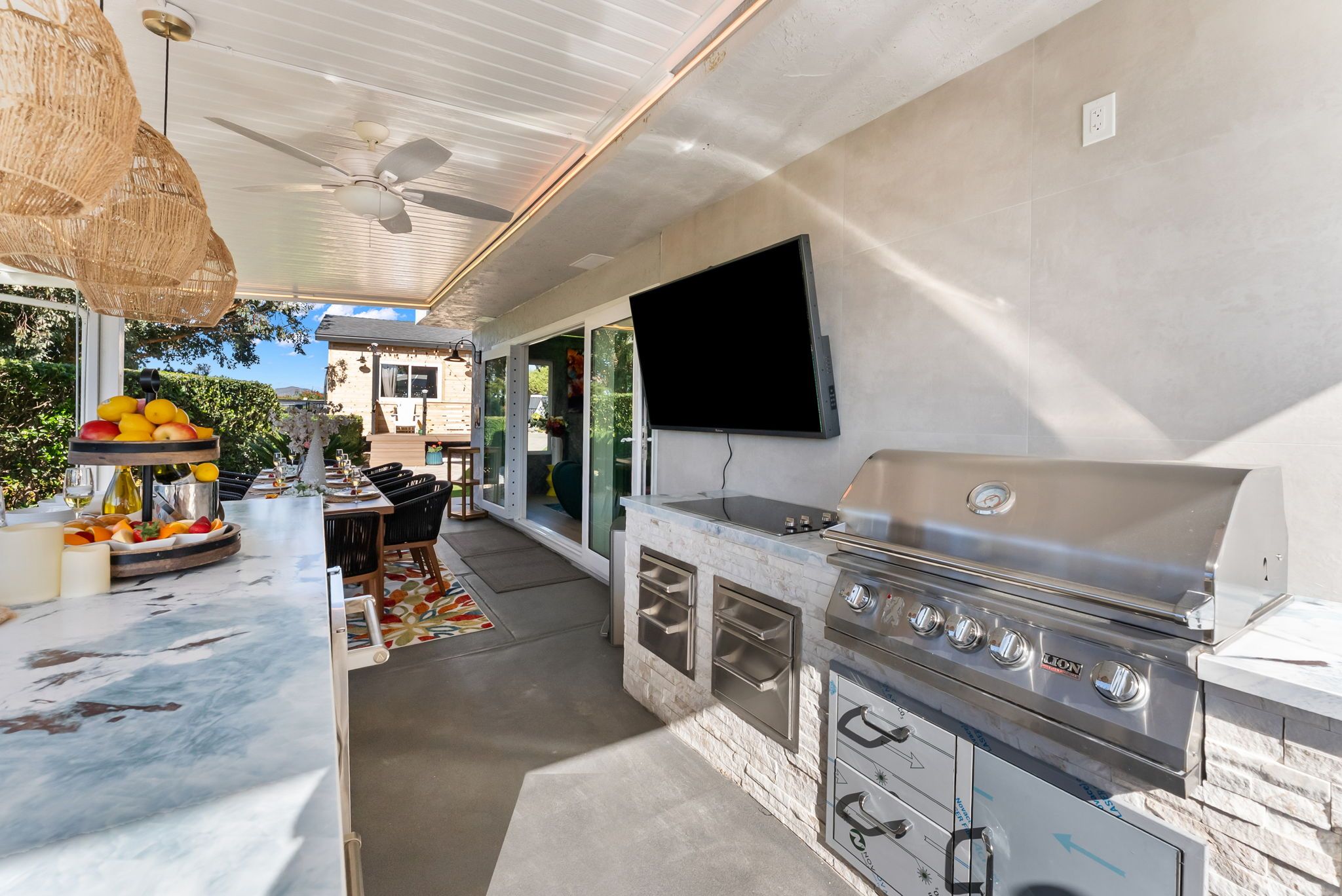 An outdoor kitchen area with a grill, a dining table with chairs, and a fruit display.