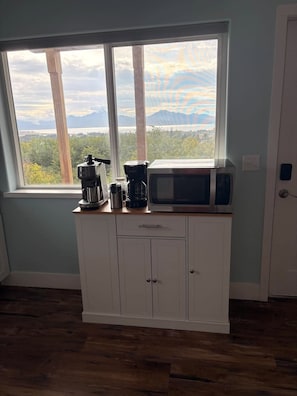 Ett kök med utsikt över bergen genom ett stort fönster, en mikrovågsugn och en kaffebryggare på bänkskivan.