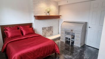 A bedroom with a bed, a desk, a ceiling fan, a fireplace, and a door.