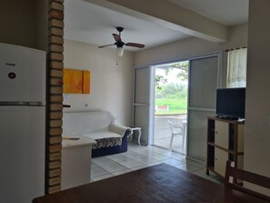 Een knus woongedeelte met een kitchenette, een plafondventilator, een bank, een eettafel en een televisie op een standaard.
