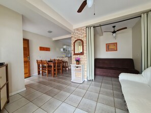 A living room with a sofa, a dining area with a table and chairs, a kitchen with a microwave, and a ceiling fan.