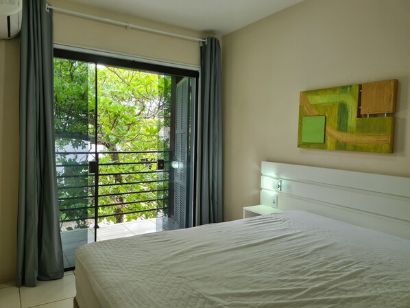 A bedroom with a bed, a window with curtains, a nightstand, and a wall-mounted painting.