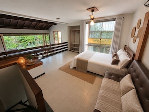 A hotel room with a bed, a sofa, a desk, and a balcony with a view of greenery. - Bahia Beira Mar Hotel (Porto Seguro)