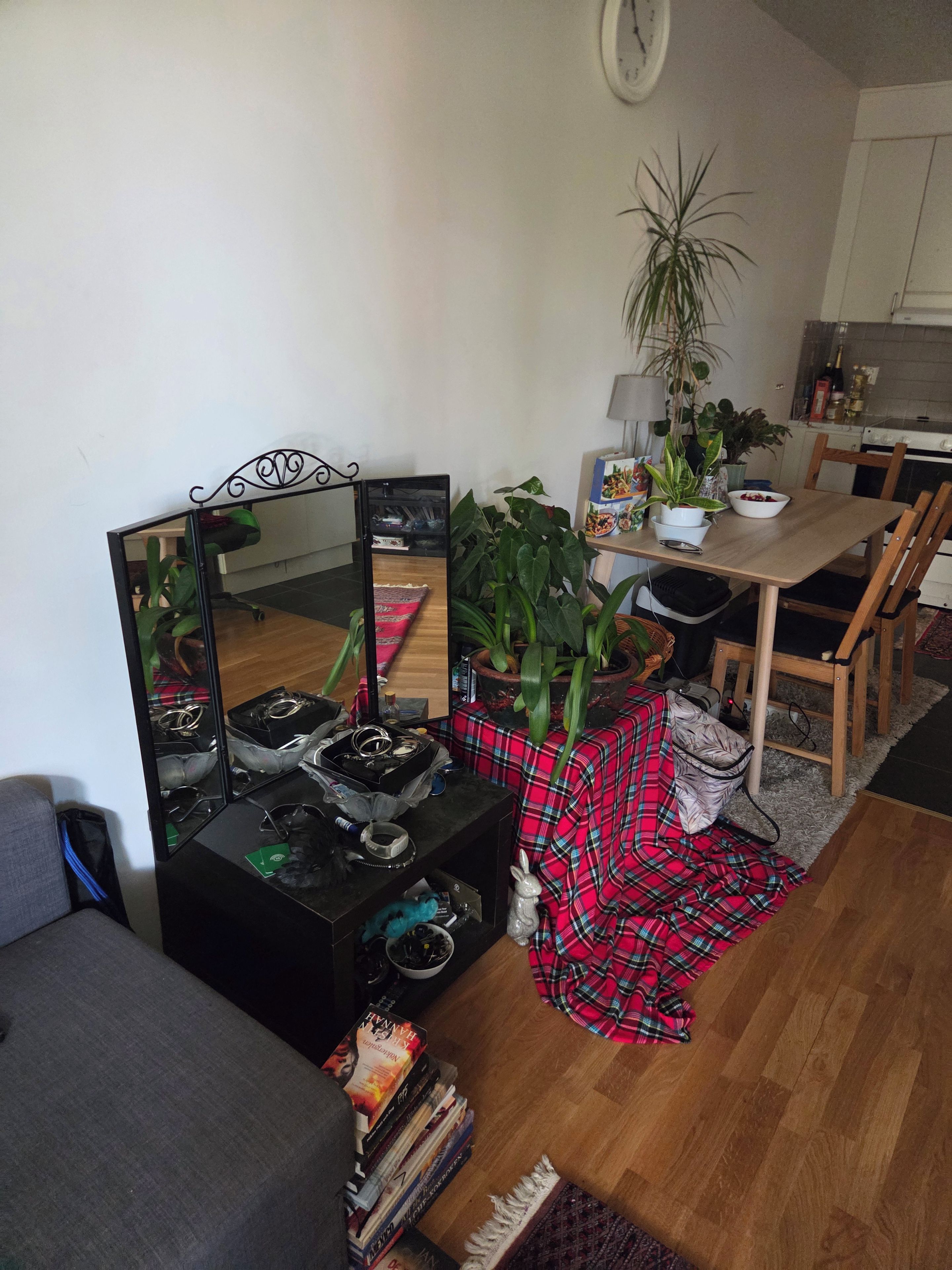Un salon comprenant un canapé, une table basse recouverte d’une nappe à carreaux rouges, un miroir et un coin repas avec une table et des chaises en bois.