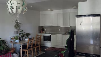 Cozinha moderna com armários brancos, geladeira de aço inoxidável e área de refeições com mesa e cadeiras de madeira.