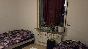 A bedroom with two single beds, a window with a curtain, a radiator, and a potted plant. - Luxury Apartment - The subway is right outside the apartment (Stockholms län)