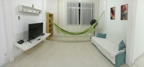 Ein Wohnzimmer mit Fernseher, Hängematte, Sofa und Heizkörper.