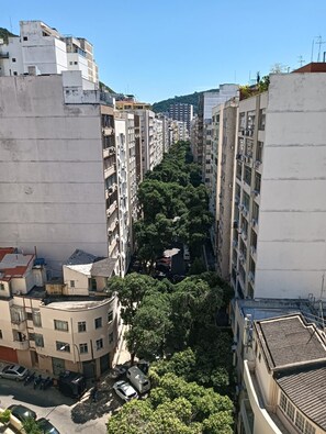 Eine schmale Stadtstraße, gesäumt von mehrstöckigen Wohnhäusern mit Balkonen, Bäumen und abgestellten Fahrzeugen.