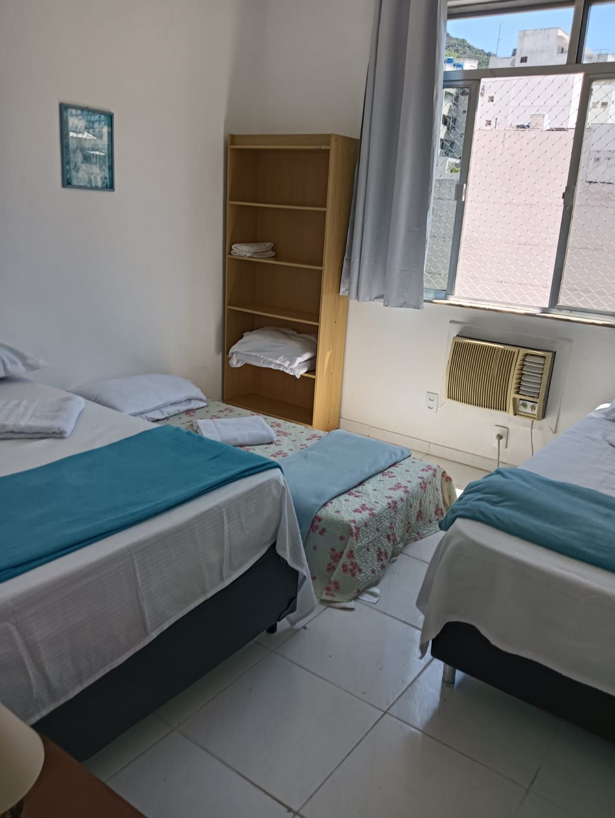 Habitación con dos camas, un armario de madera, un radiador y una ventana con vistas a edificios.