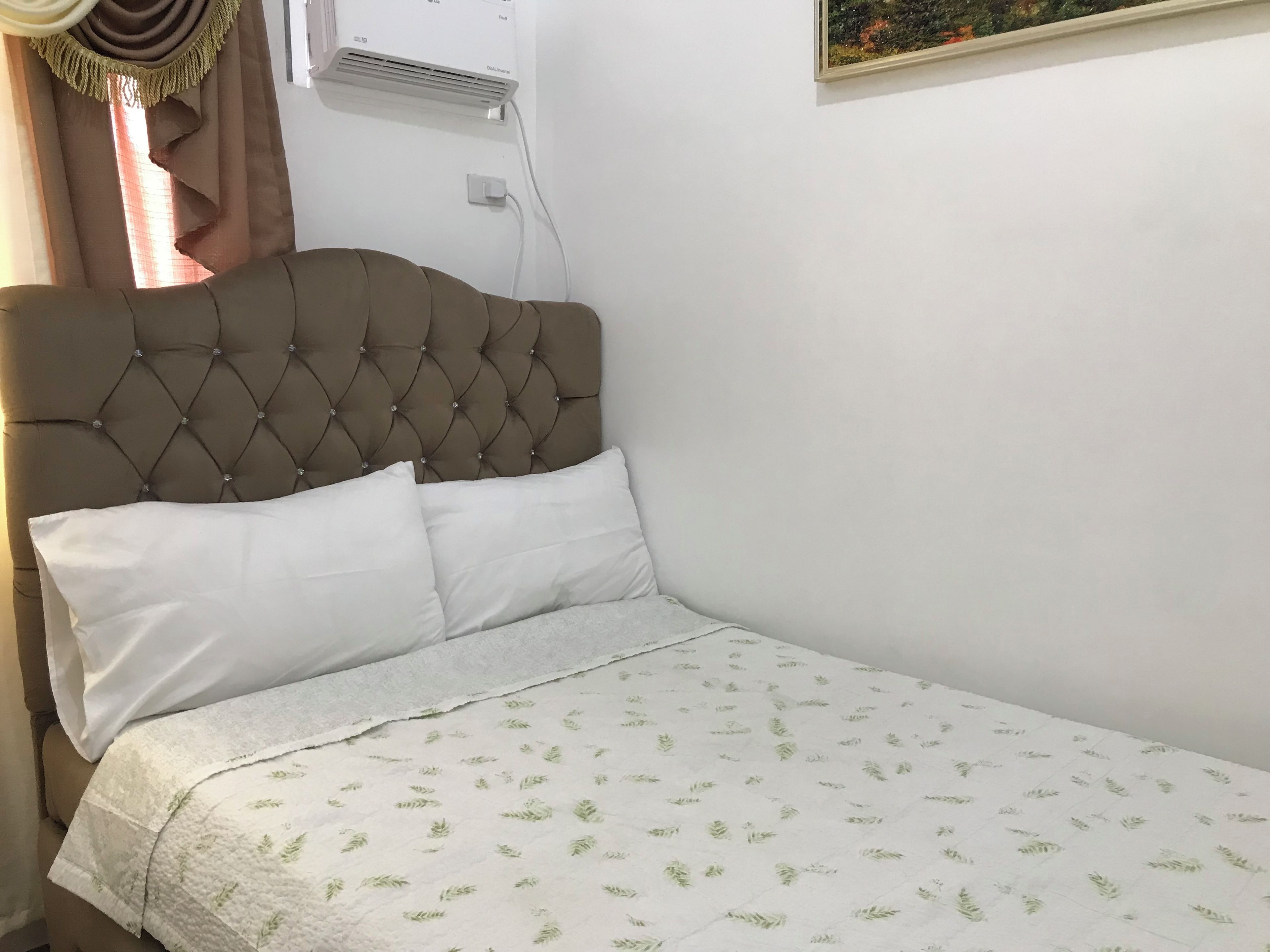 A bed with a tufted headboard, white pillows, and a leaf-patterned bedspread.