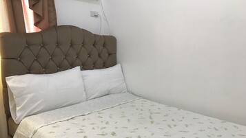 A bed with a tufted headboard, white pillows, and a leaf-patterned bedspread.