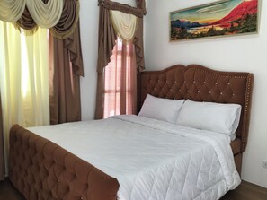 Une chambre à coucher avec un grand lit, une tête de lit capitonnée et des rideaux.