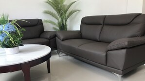 A modern living room with a dark brown leather sofa, a white round coffee table, and a potted plant with blue flowers. - Superhost Home - 2 min Airport -Pool WiFi - Samal (Davao)