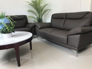 Un salon moderne avec un canapé en cuir marron foncé, une table basse ronde blanche et une plante en pot aux fleurs bleues.